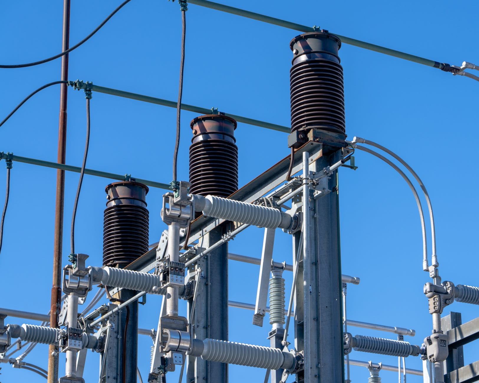 Detailed view of electrical components in a power substation under a clear blue sky.