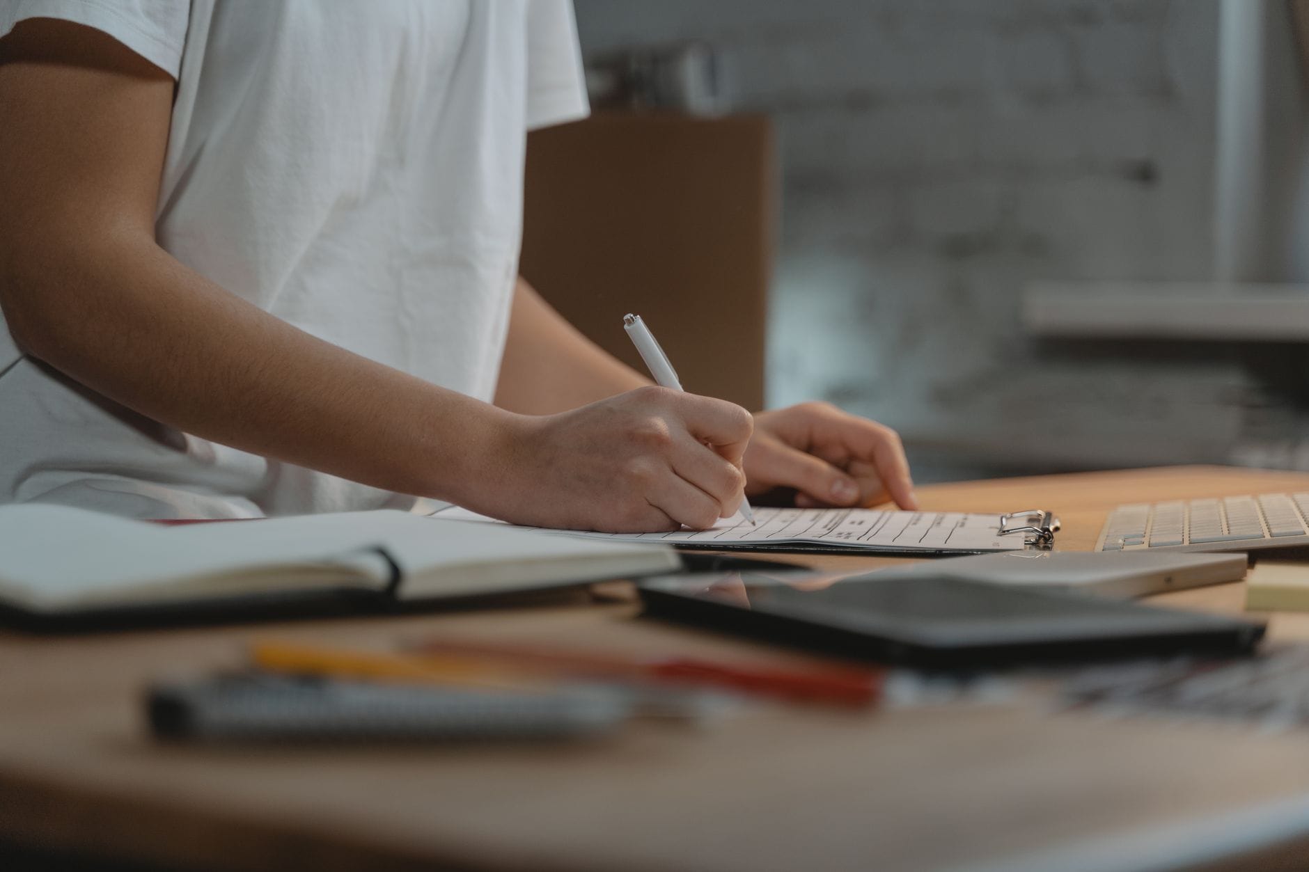 Close-up of individual writing on a clipboard at a desk with office supplies.