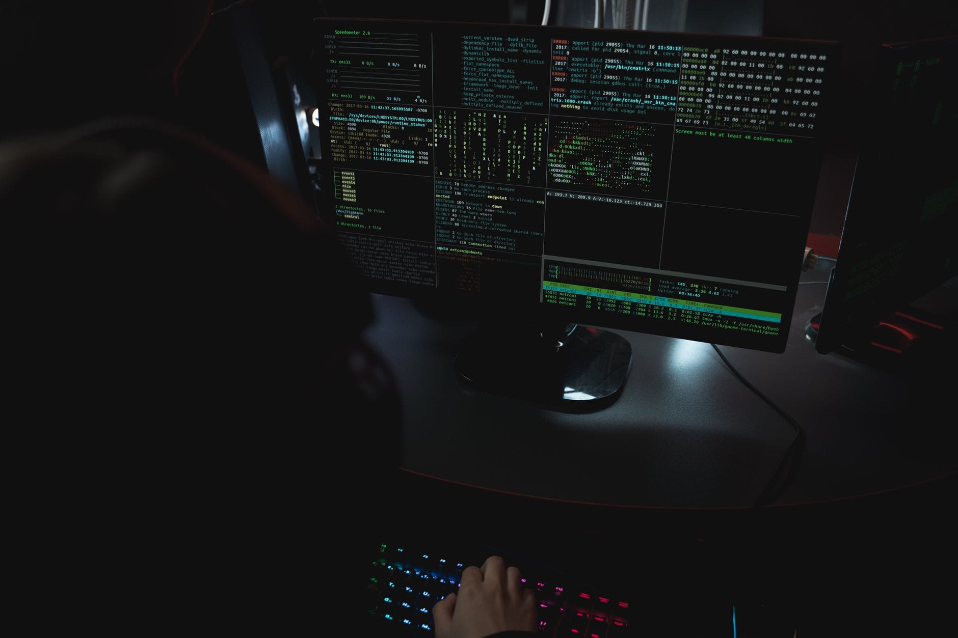 Dark room setup with code displayed on PC monitors highlighting cybersecurity themes.