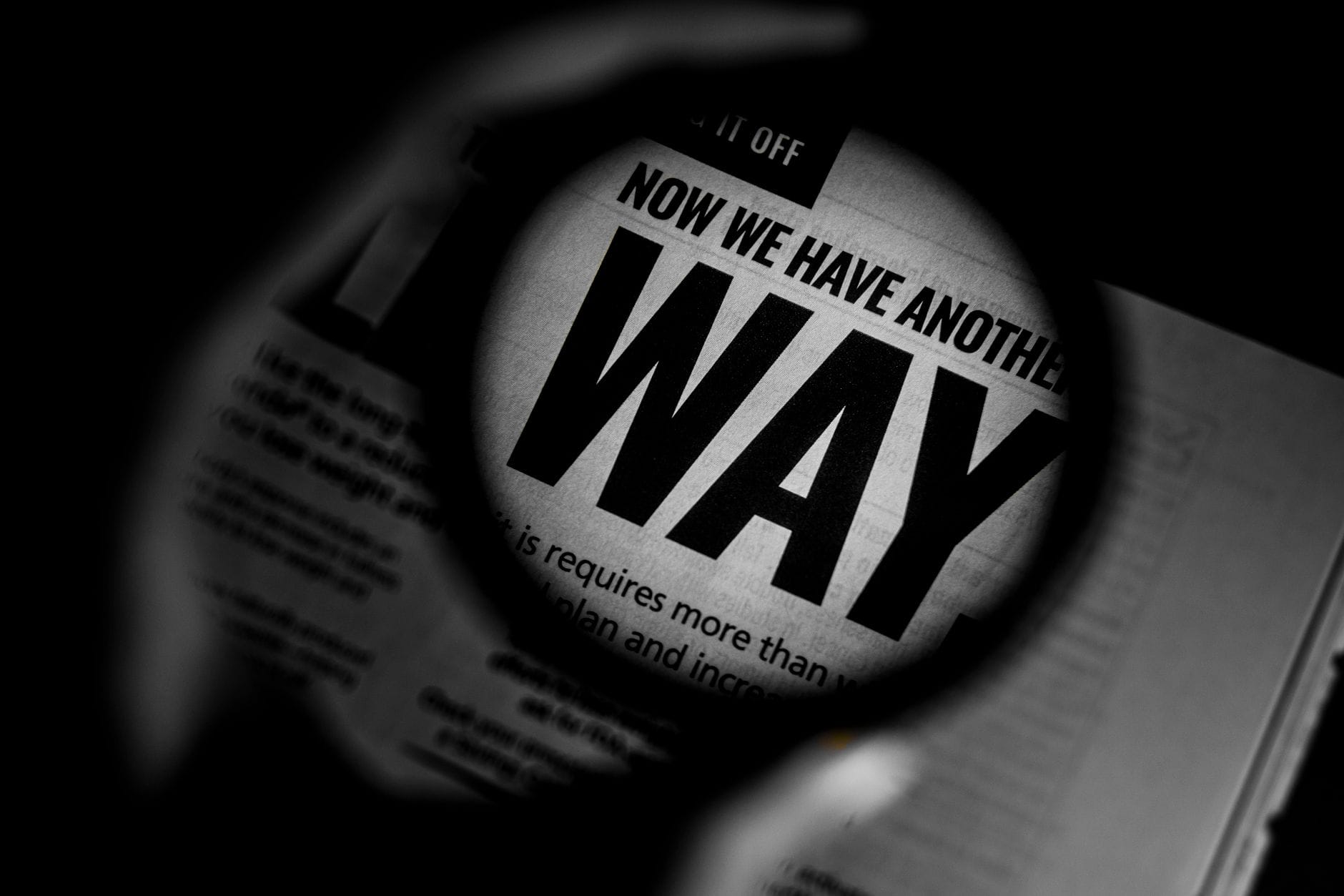 Black and white close-up of newspaper text magnified through a lens, emphasizing the word 'WAY'.