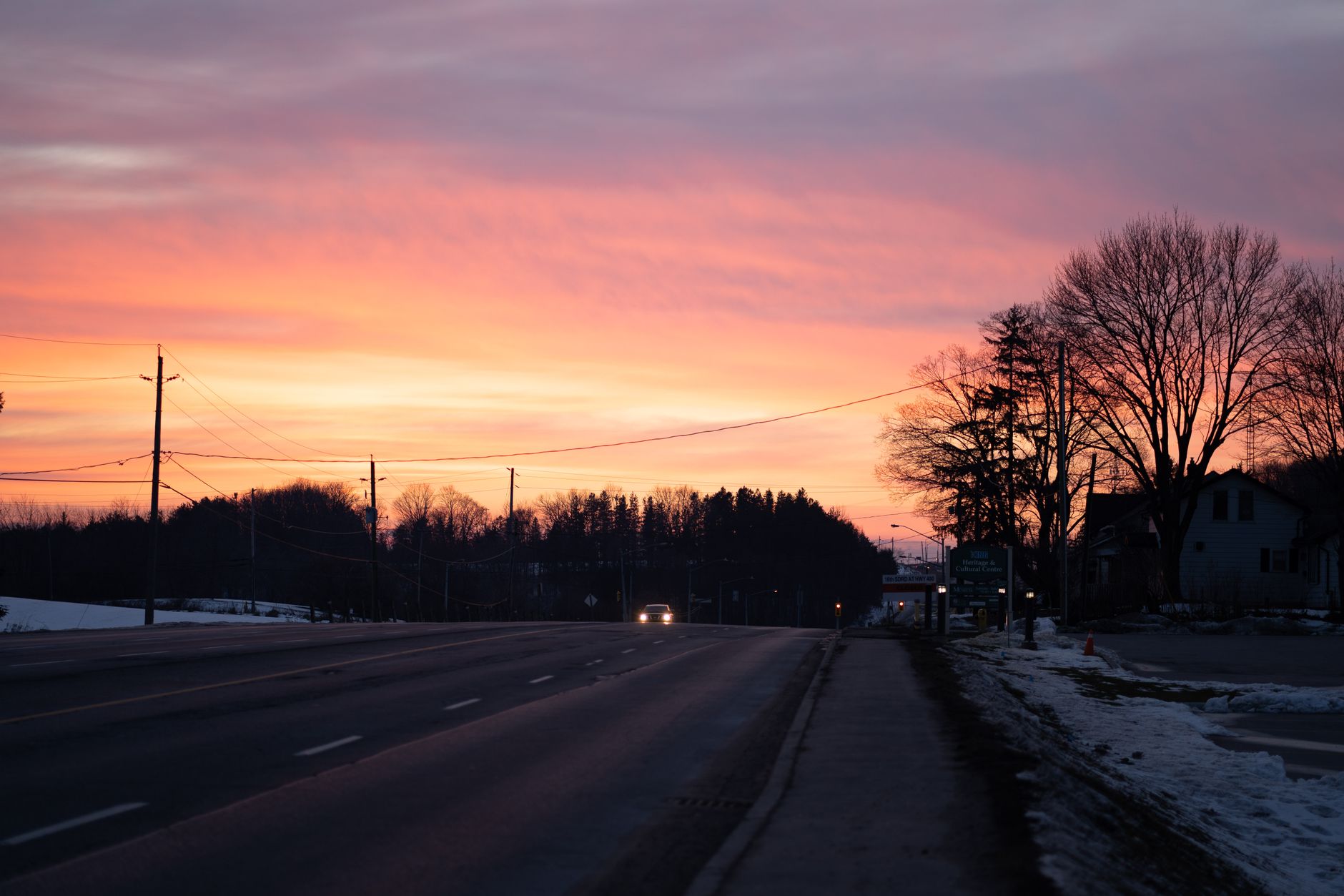 A scenic winter sunset over a road in King City, Canada, highlighting silhouettes of trees and an orange sky.